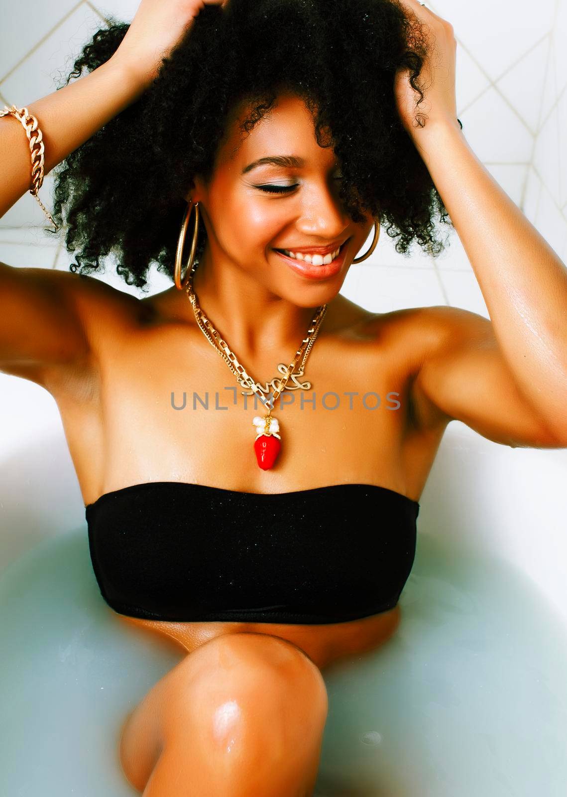 young afro-american teen girl laying in bath with foam, wearing swag jewelry flawless, making selfie close up