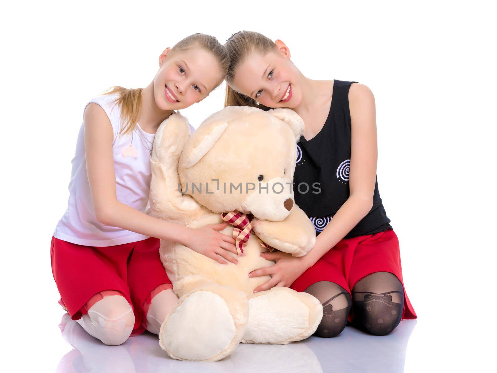 Lovely little girls. Next to a large teddy bear on a white background in the studio. The concept of holidays, happy childhood. Isolated.