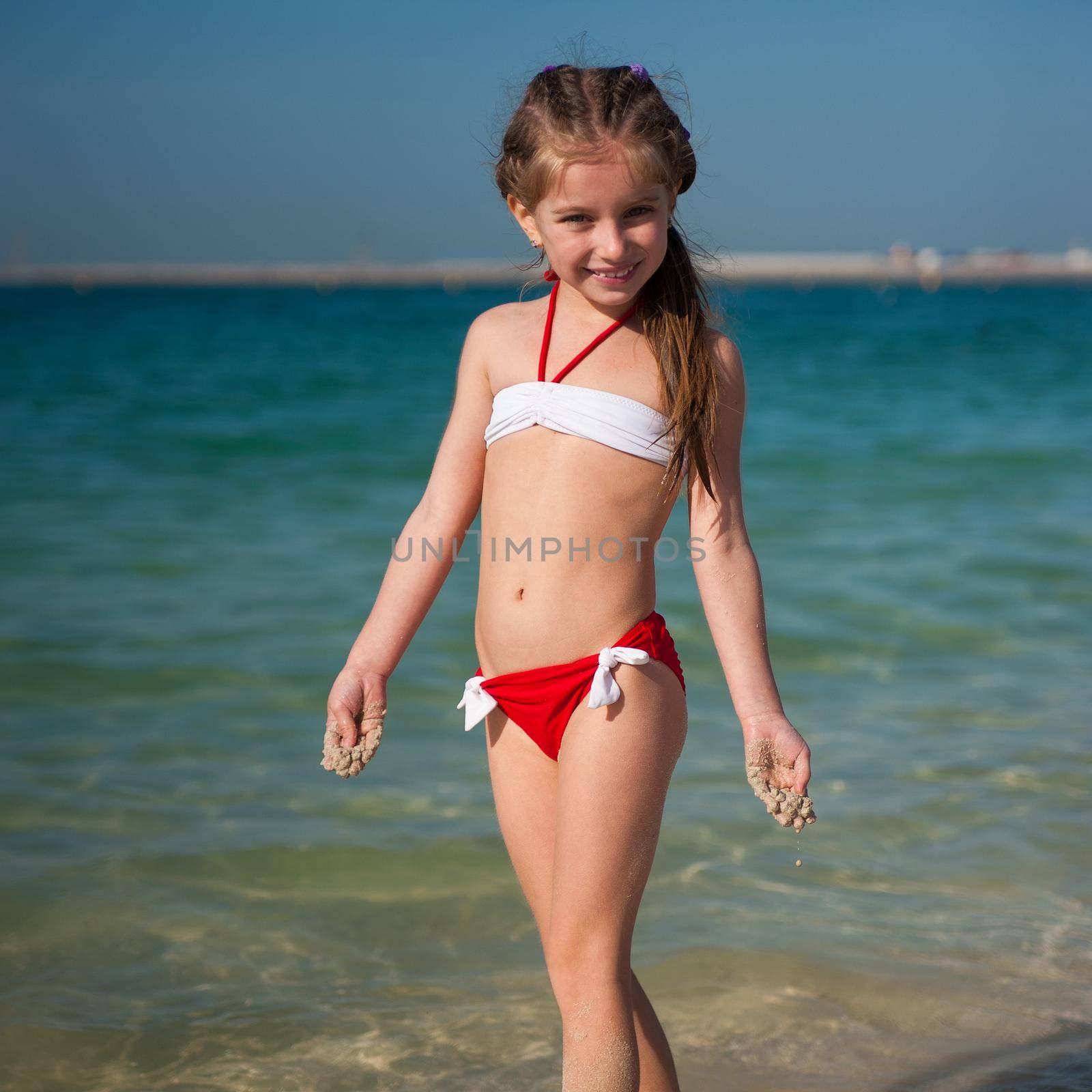 cute little girl in red-and-white swimsuit on the beach