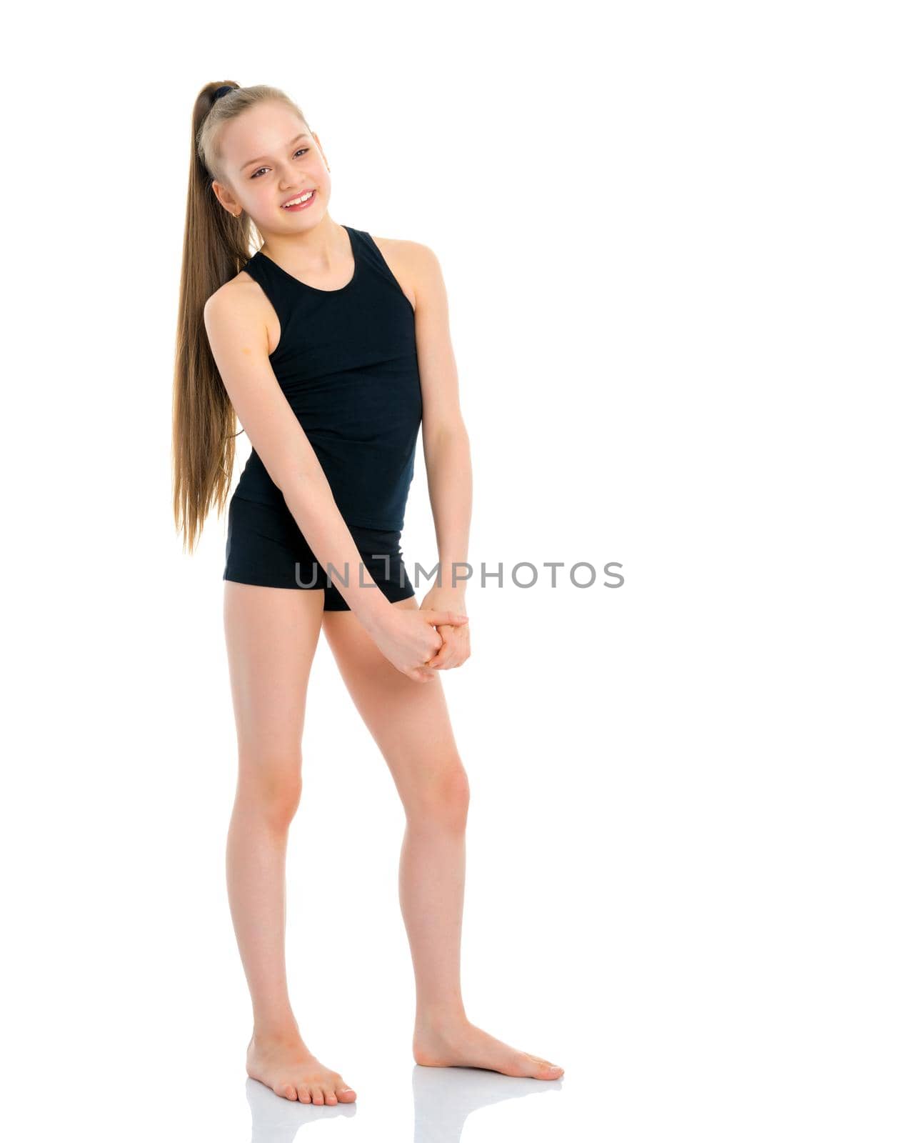 A beautiful girl gymnast of school age in a black T-shirt and shorts is preparing for the exercise. The concept of sport and fitness, happy people. Isolated on white background.