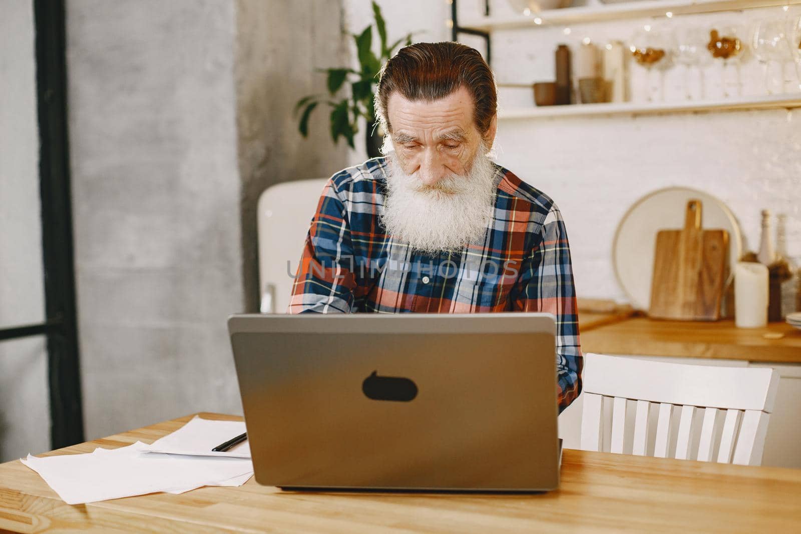 Old man with laptop. Grandfather sitting in a Christmas decorations. Man in a cell shirt.