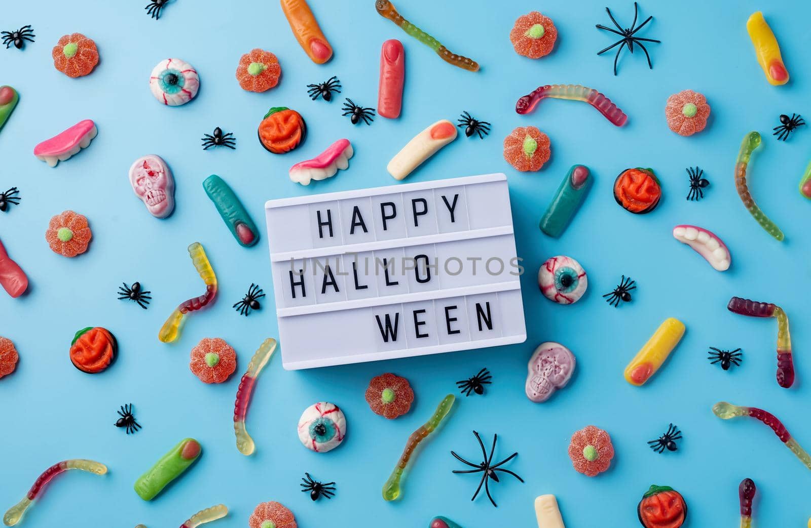 Halloween holiday decorations and sweets with lightbox with words Happy Halloween flat lay on blue background by Desperada