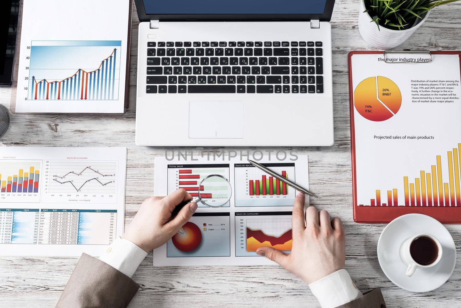 Businessman working with financial report in office. Flat lay wooden desk with laptop, business diagrams and cup of coffee. Top view office workplace with human hands. Stock market analysis concept