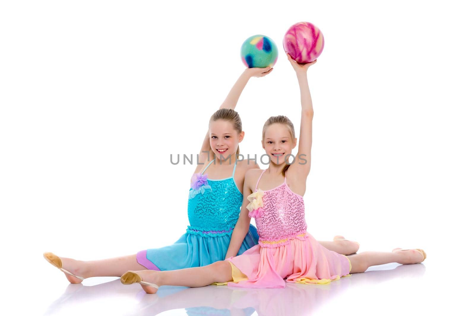 Two cheerful little girls gymnasts in competitions, perform exercises with the ball. The concept of children's sports, fitness, healthy lifestyle. Isolated on white background.