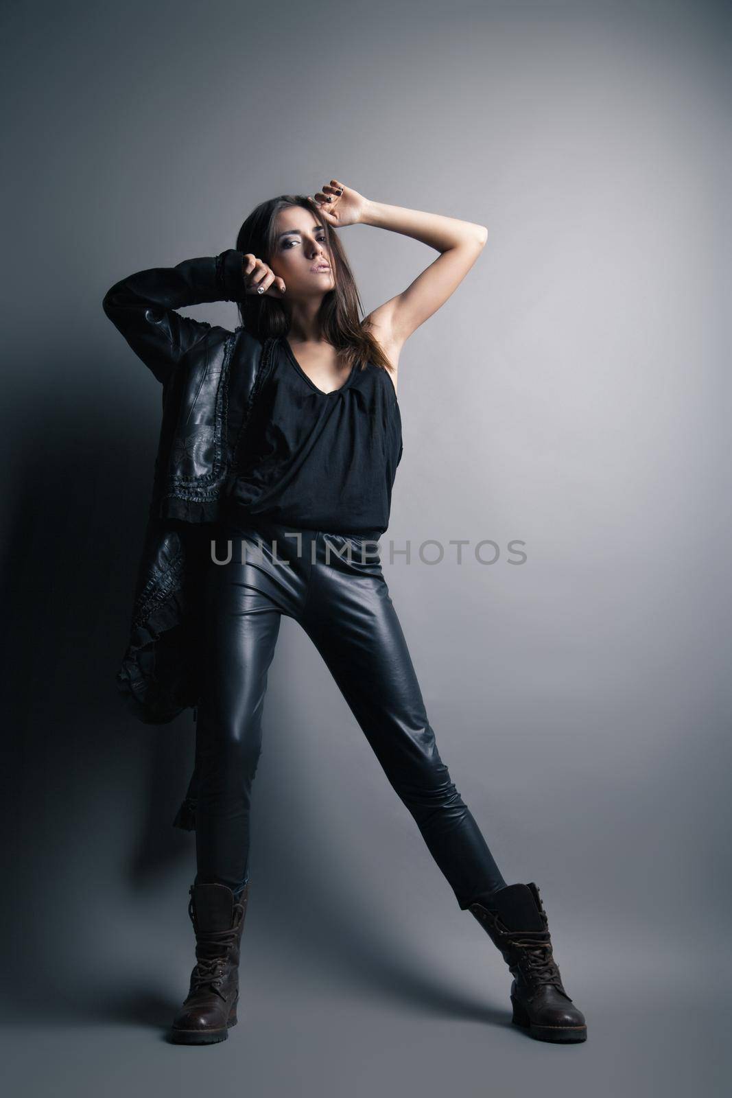 Fashion model wearing leather pants and jacket posing on grey background