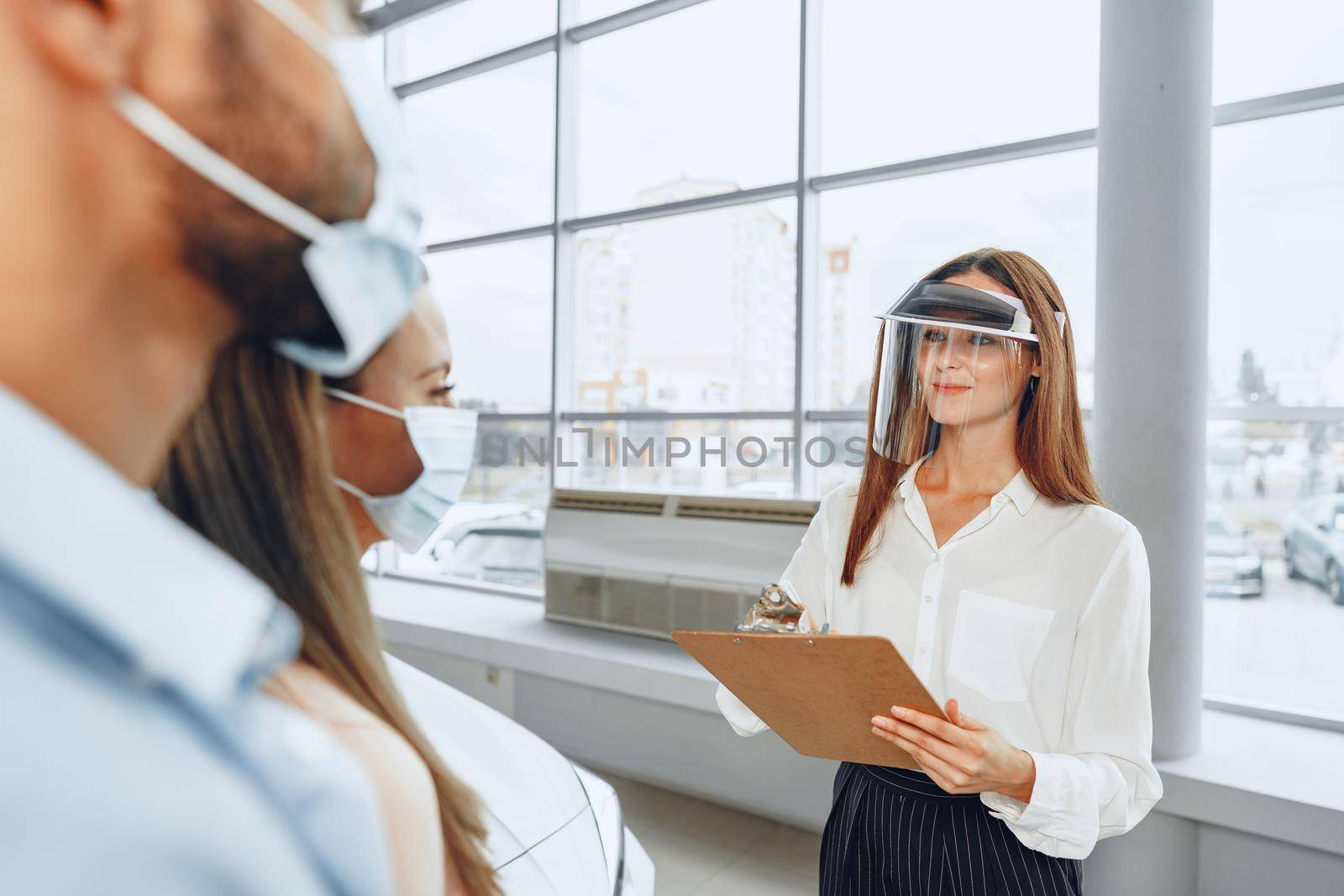 Woman car dealer consulting buyers wearing medical face shield. Coronavirus job requirements concept