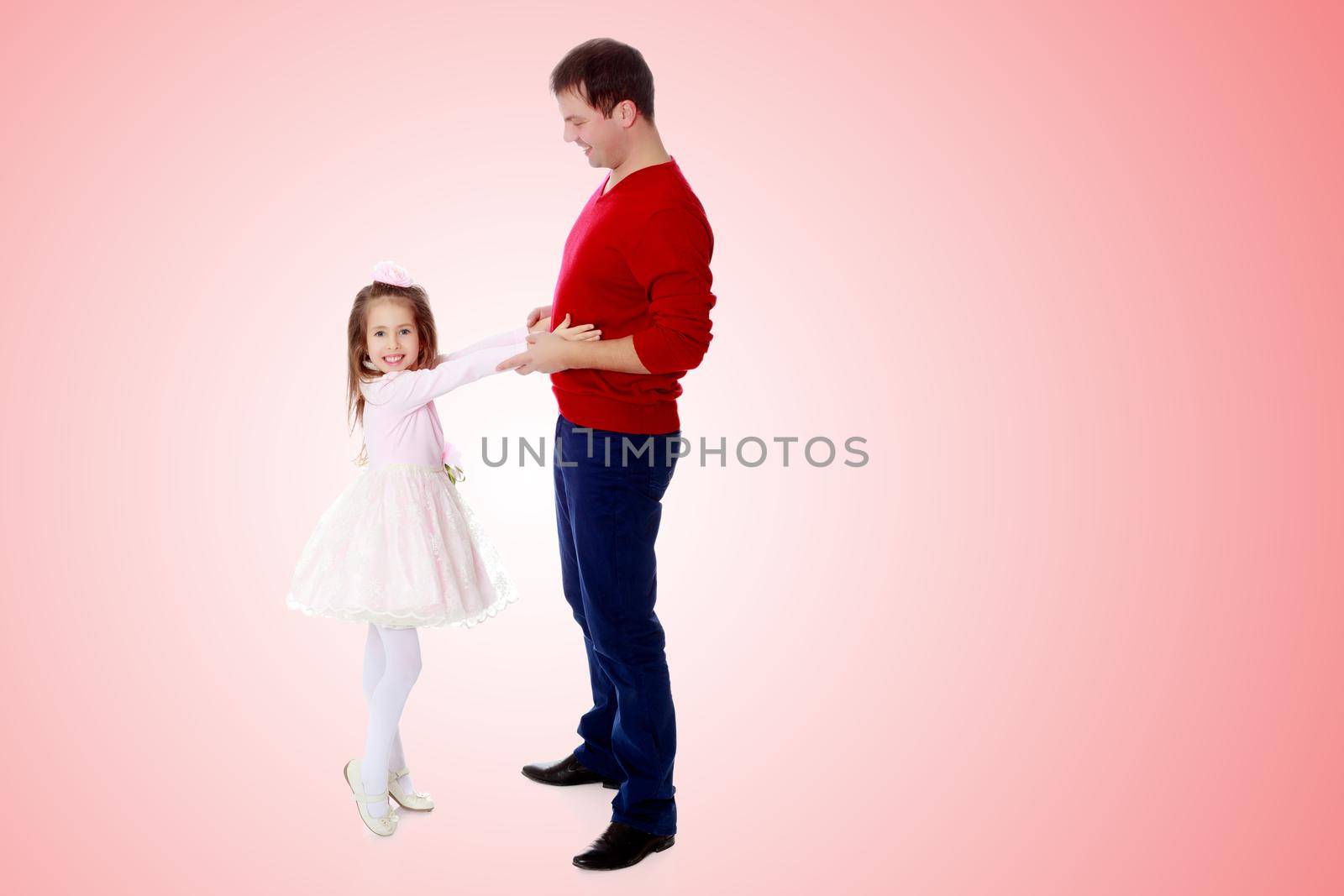 Cute little long-haired girl in a smart pink dress , reaches out to his dad.Pale pink gradient background.