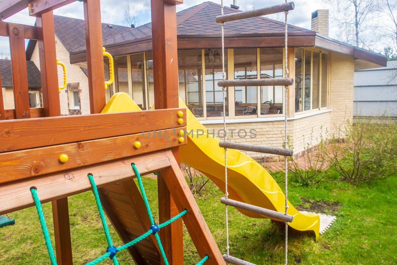 A fragment of a children's play complex with a hill and a rope ladder against the background of a summer gazebo.