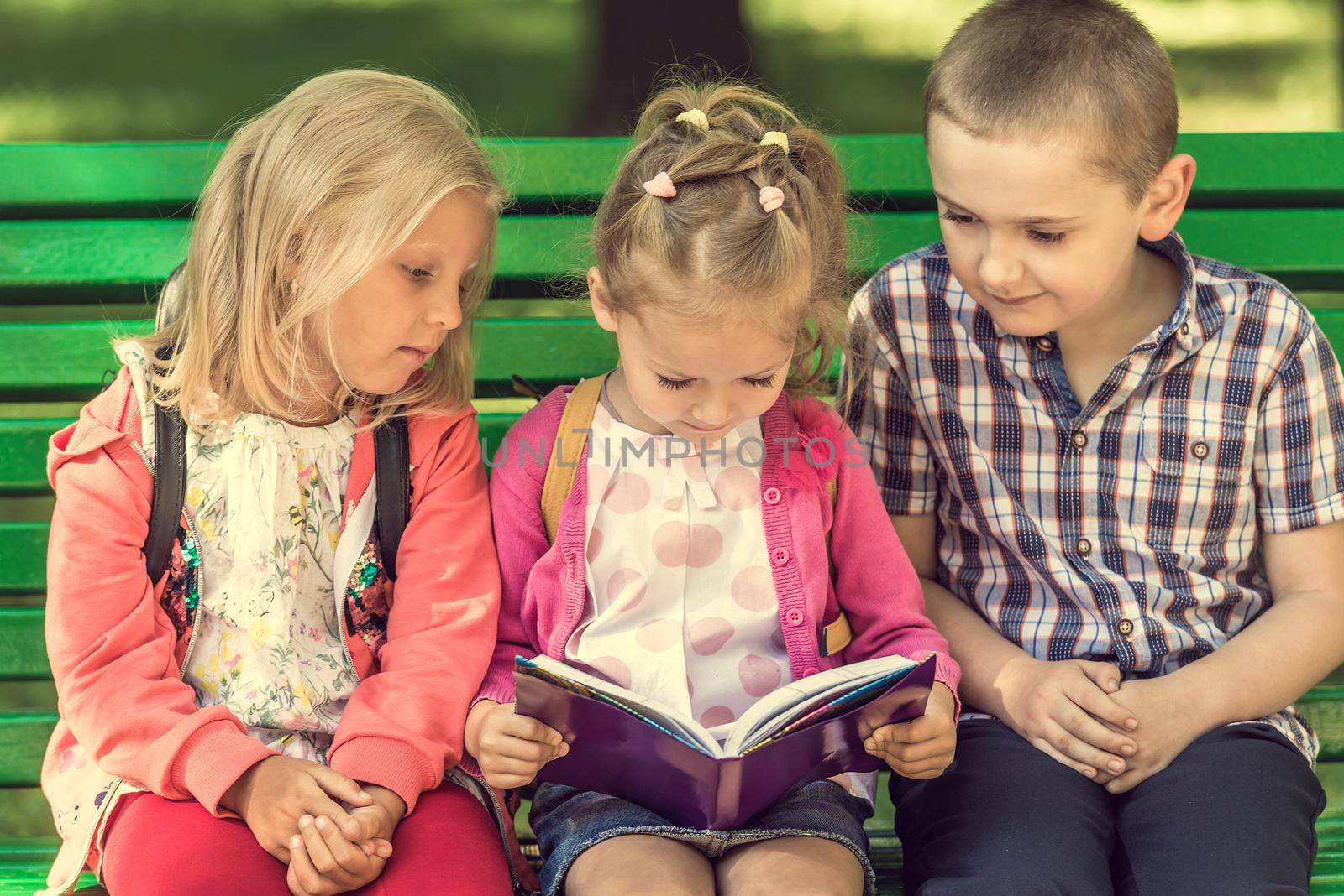 Little kids watching notes on the green bench in sunshine park