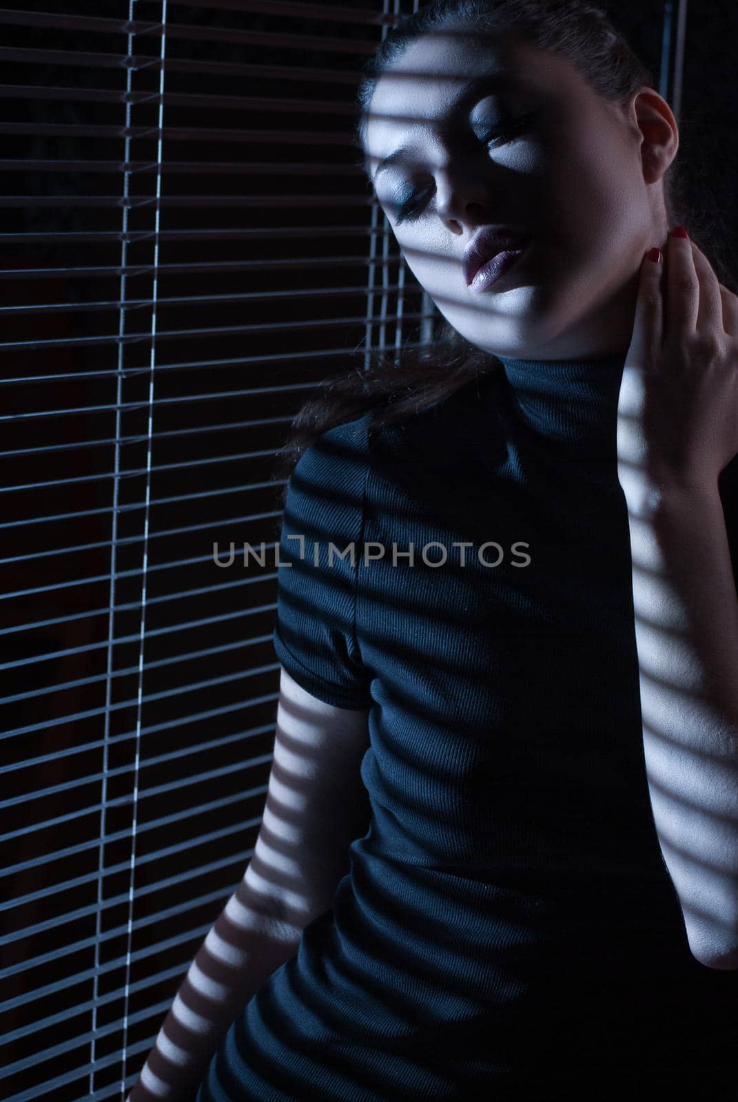 Sexy woman in black dress with jalousie looking through the window with jalousie