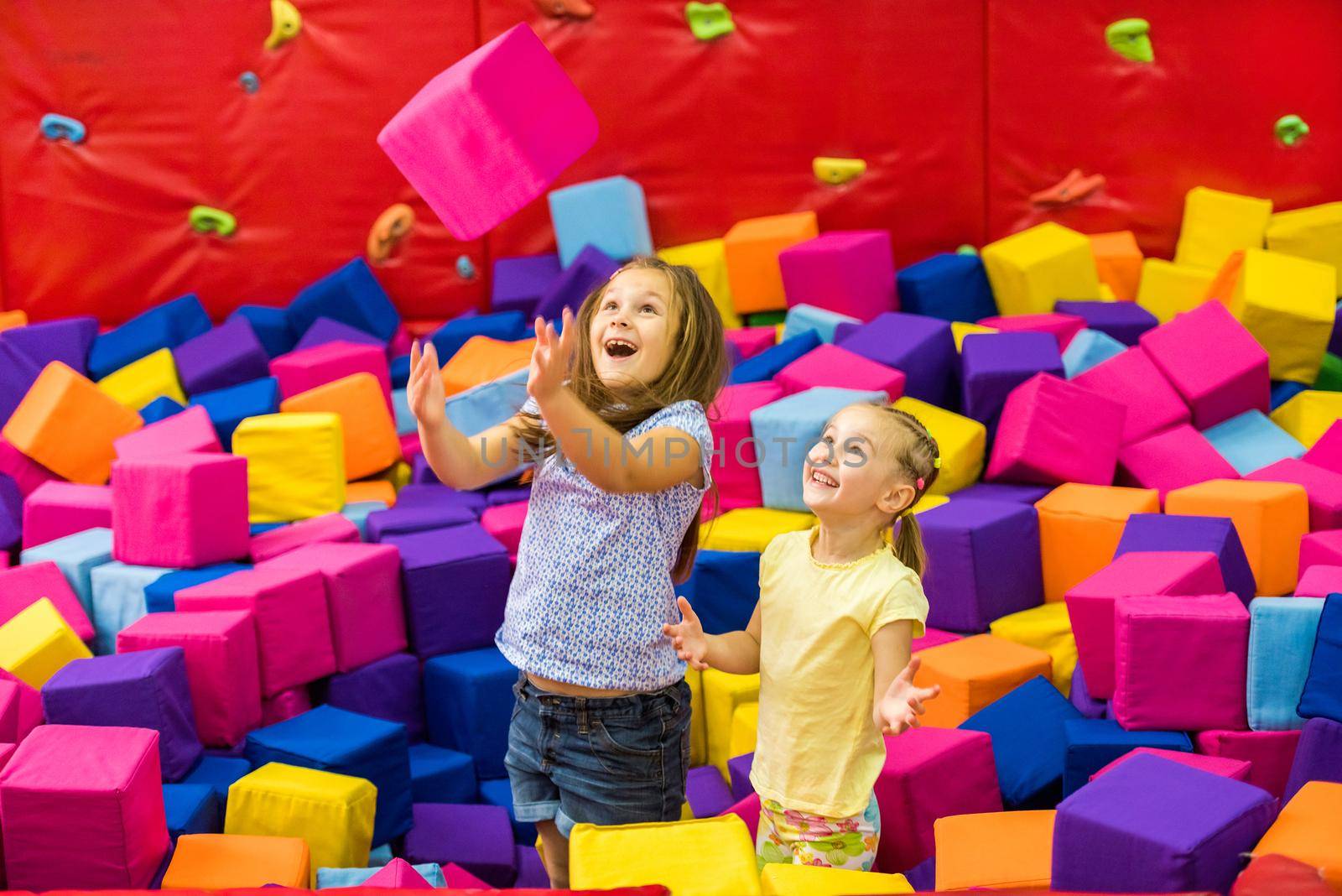 Little smiling girls playing with colourful sotf cubes in the amusement park