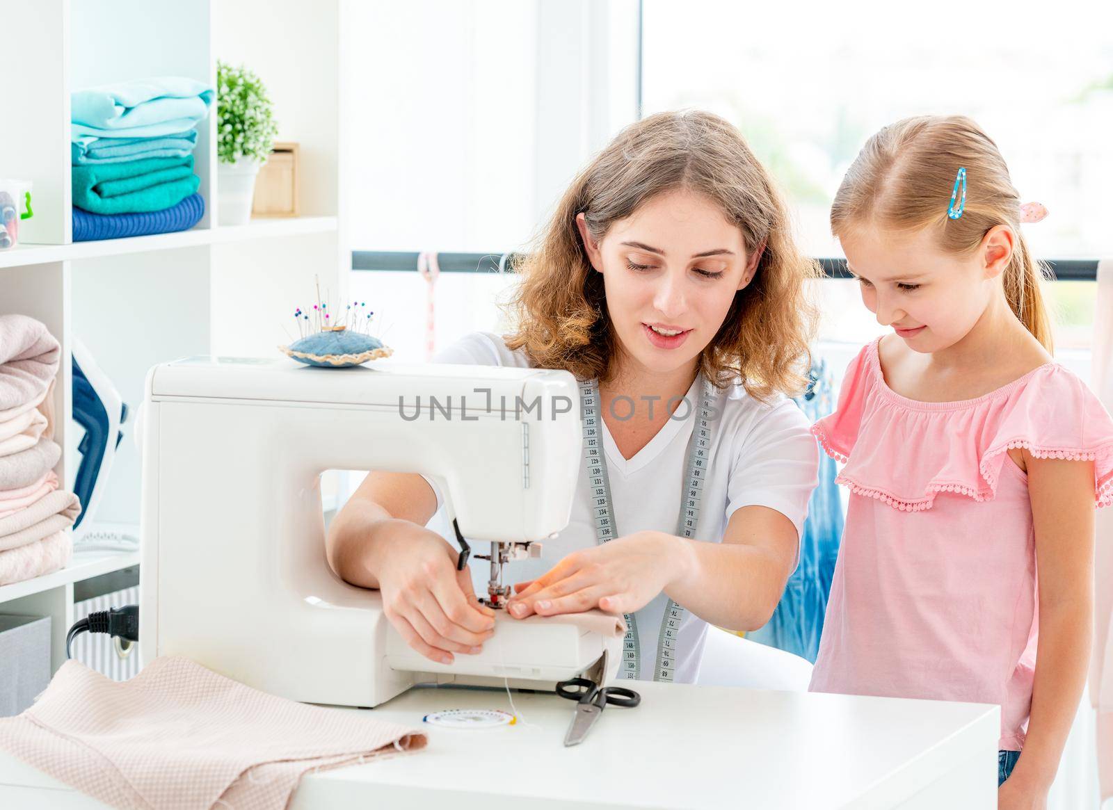 Little girl is taught to sew by teacher at class