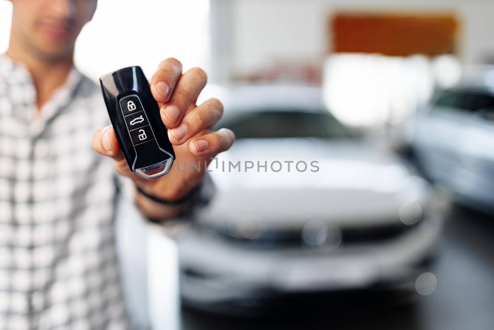 Male hand showing car keys against new luxury car in dealership