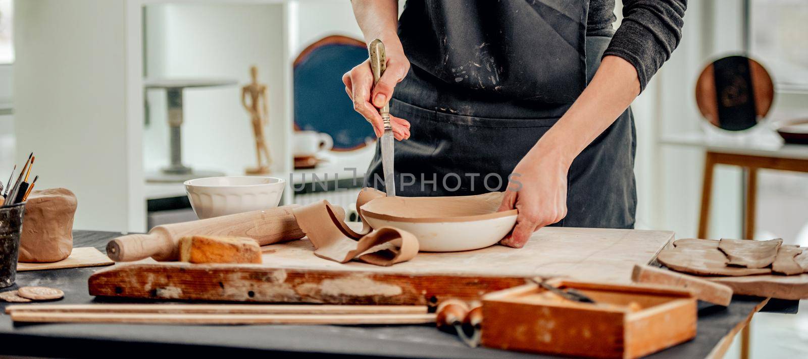 Woman using knife for plate forming from clay at pottery workshop
