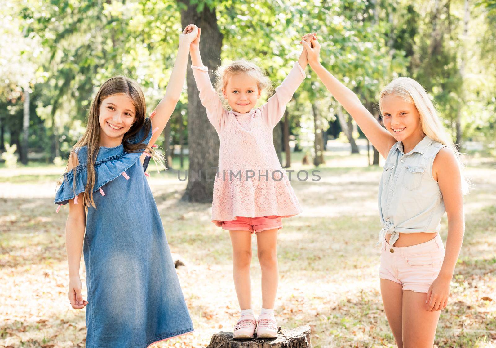 Pretty smiling little girls stand with joyfully raised hands in a sunshine autumn park