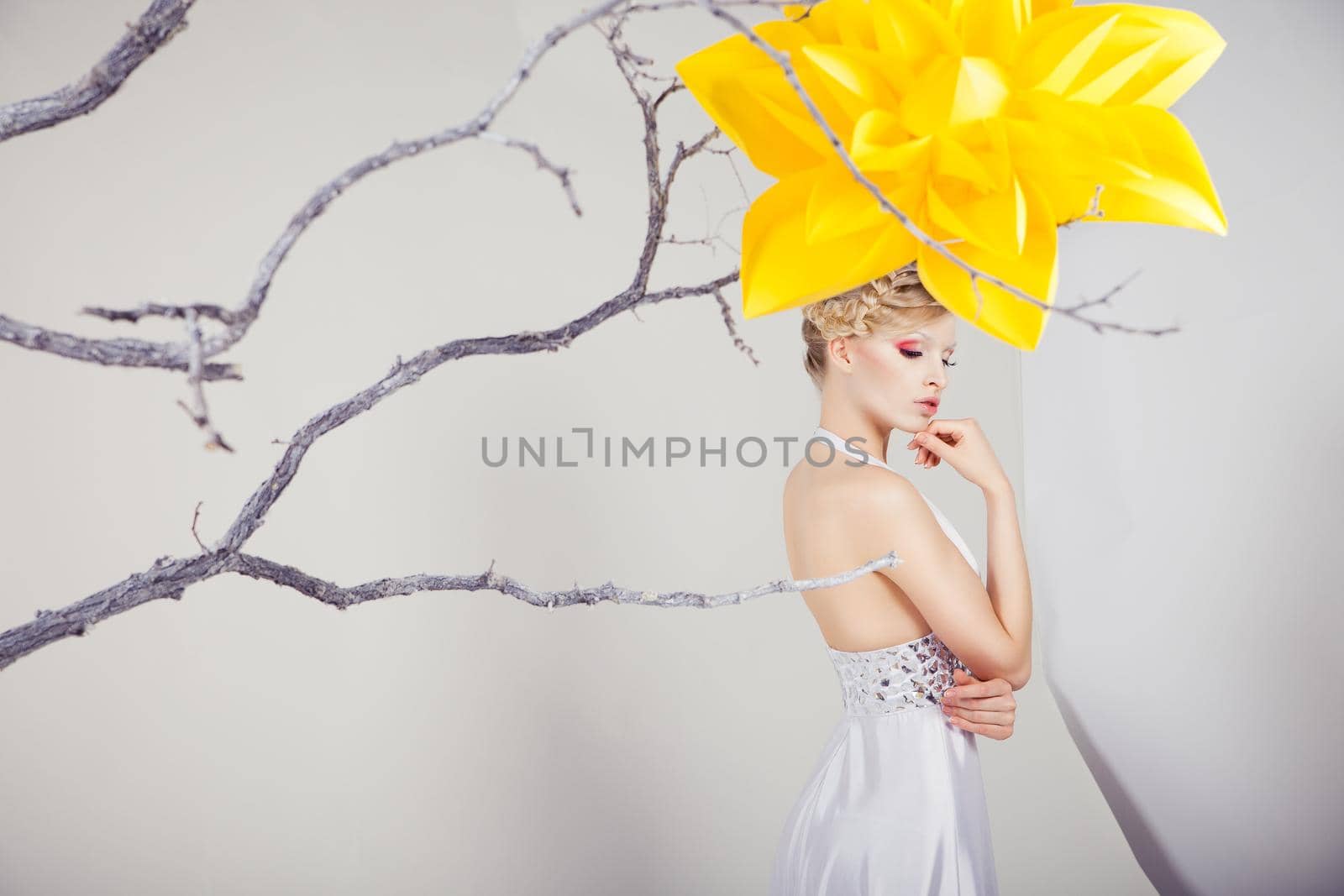 Beautiful young blond woman in white dress with big yellow flower over white background