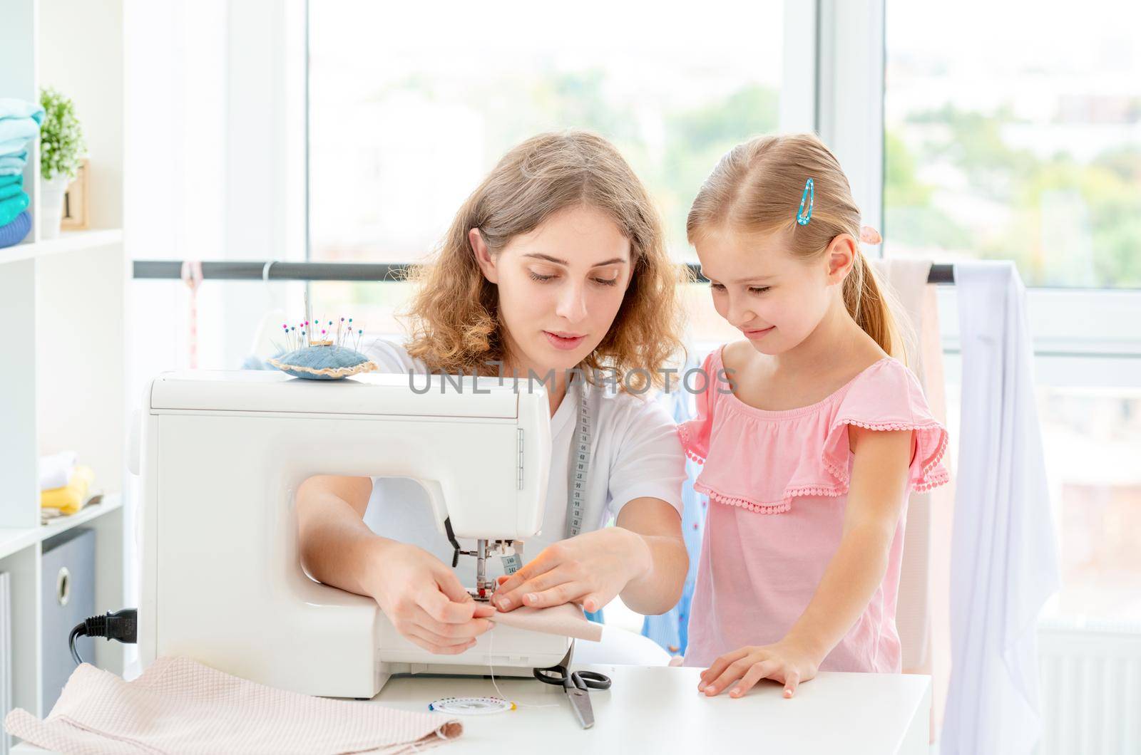 Little girl is taught to sew by teacher at class