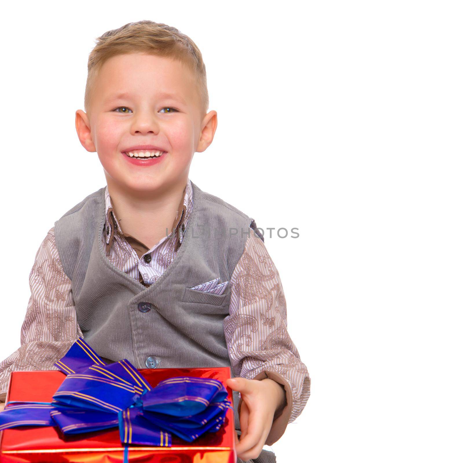 A happy little boy holds a beautifully wrapped box in which lies a gift. The concept of holidays, new year, birthday. Isolated on white background.
