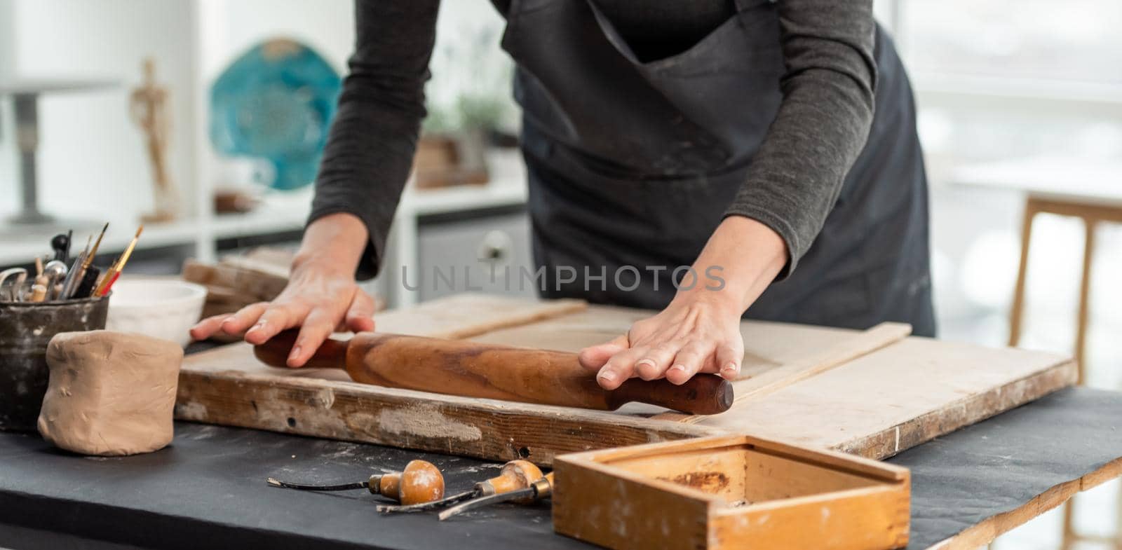 Woman using rolling pin on clay at pottery workshop, panorama