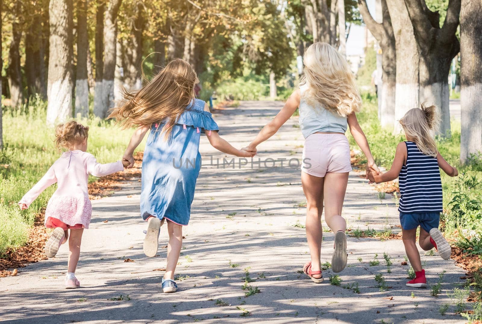 Little blond girls running on the sunshine autumn alley by holding hands