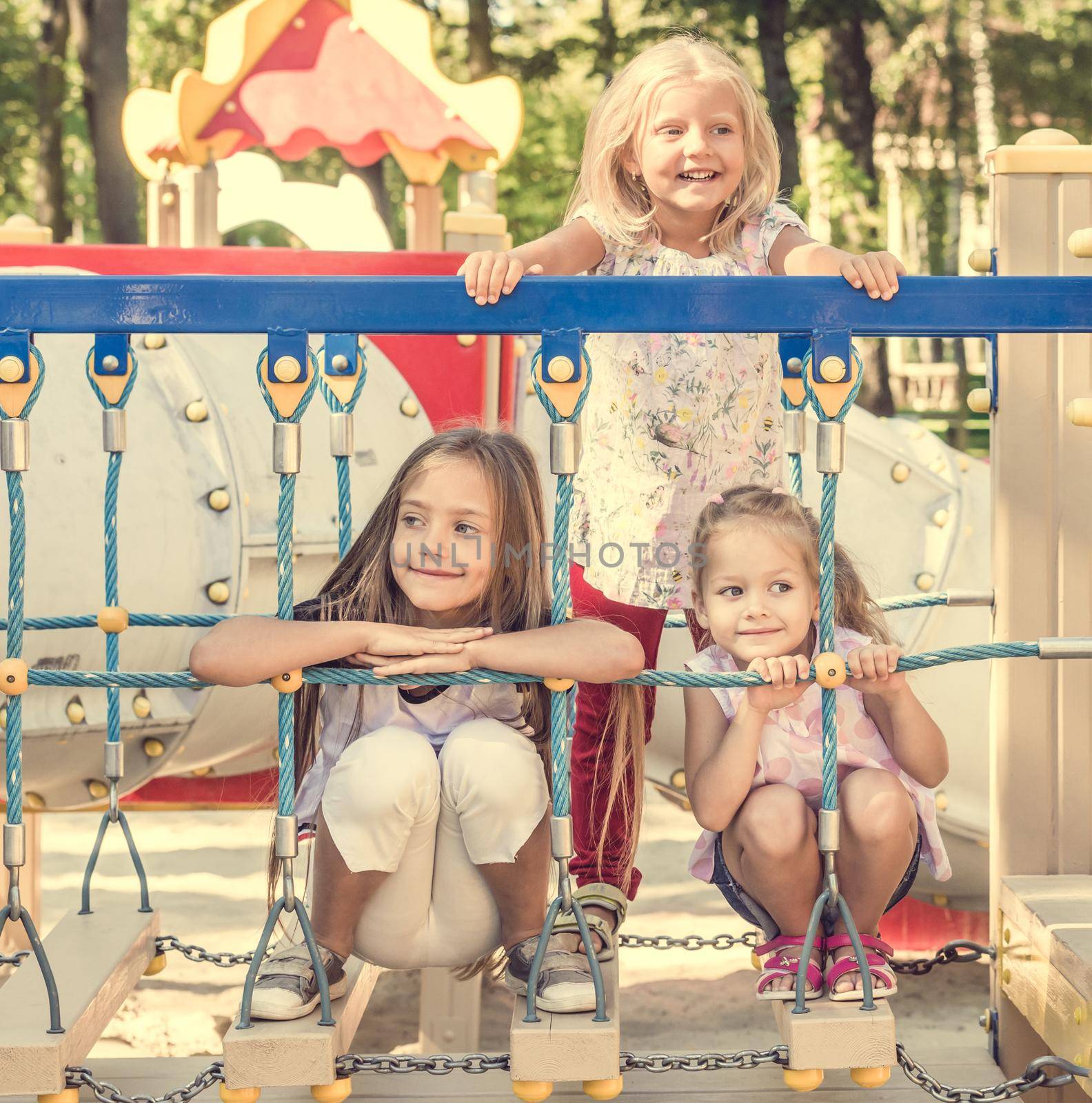 Little cute blond girls sitting on the colourful playground bridge