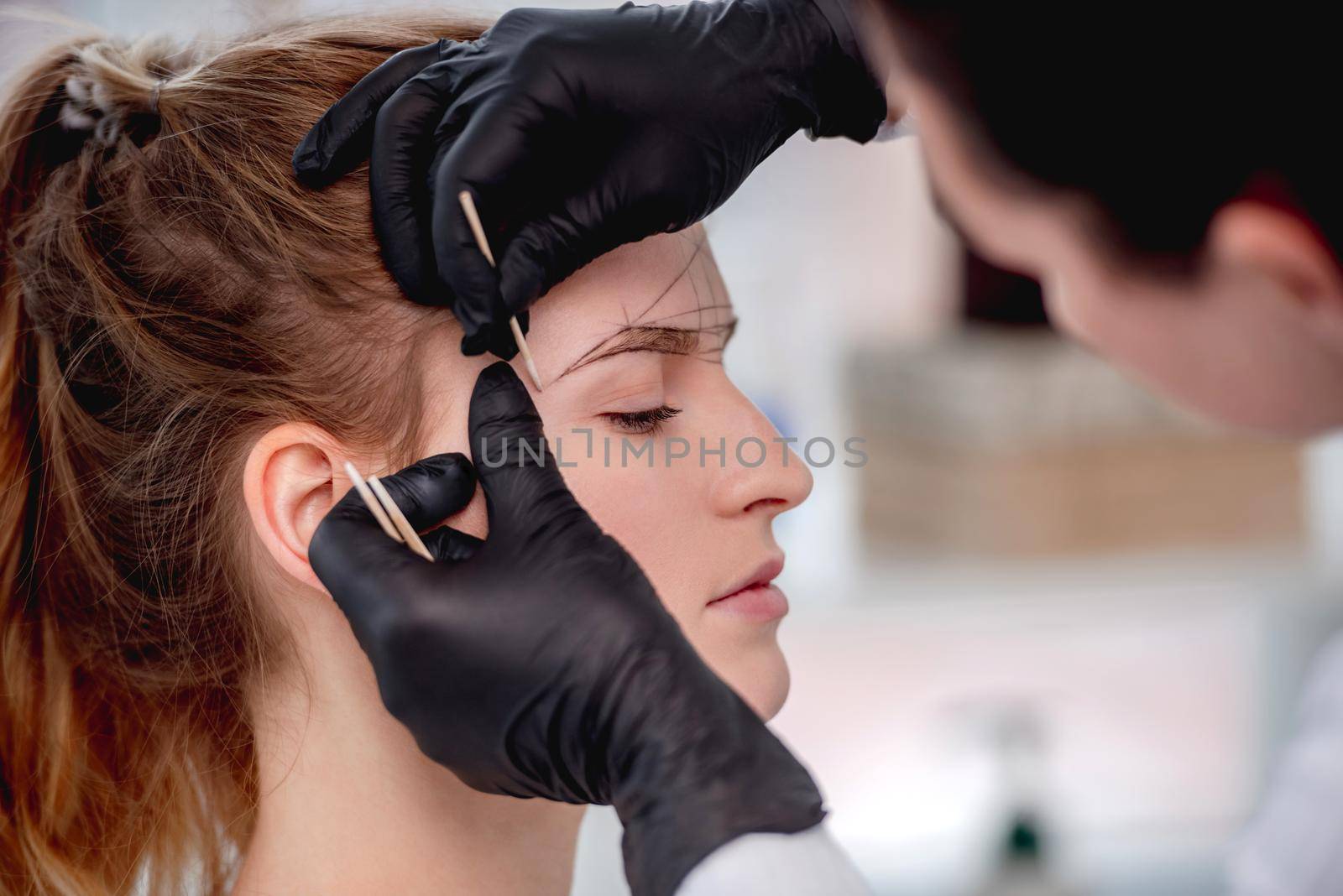 Master of microblading permanent makeup draws new shape of eyebrows for model girl. Closeup portrait of beauty tattoo process