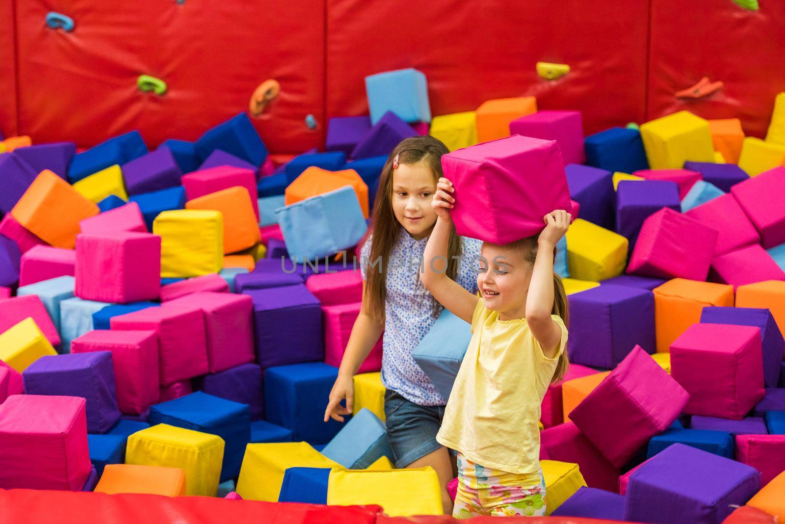 Little smiling girls playing with colourful sotf cubes in the amusement park