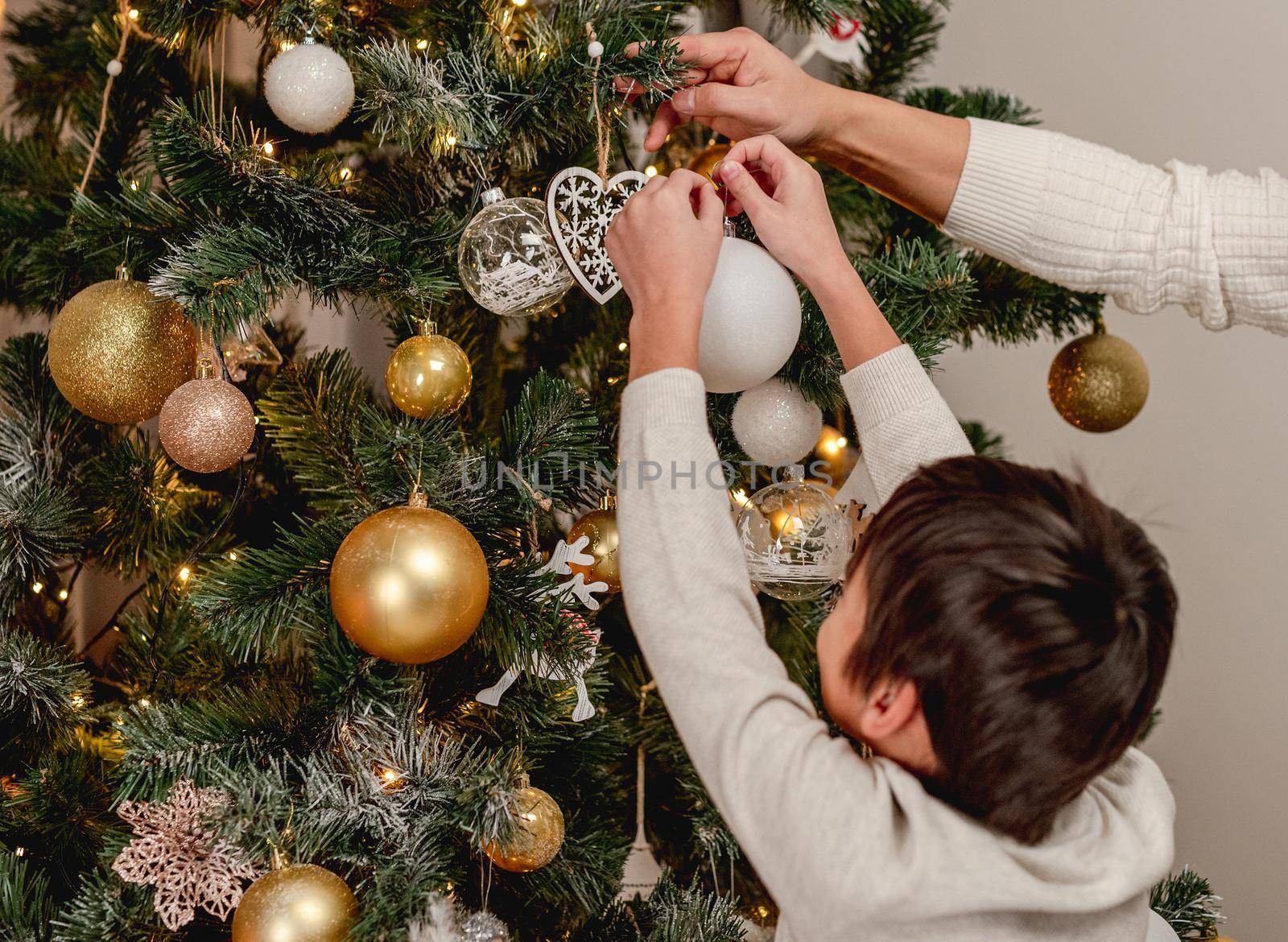 Rear view of little boy hanging decorative ball on christmas tree with father at home