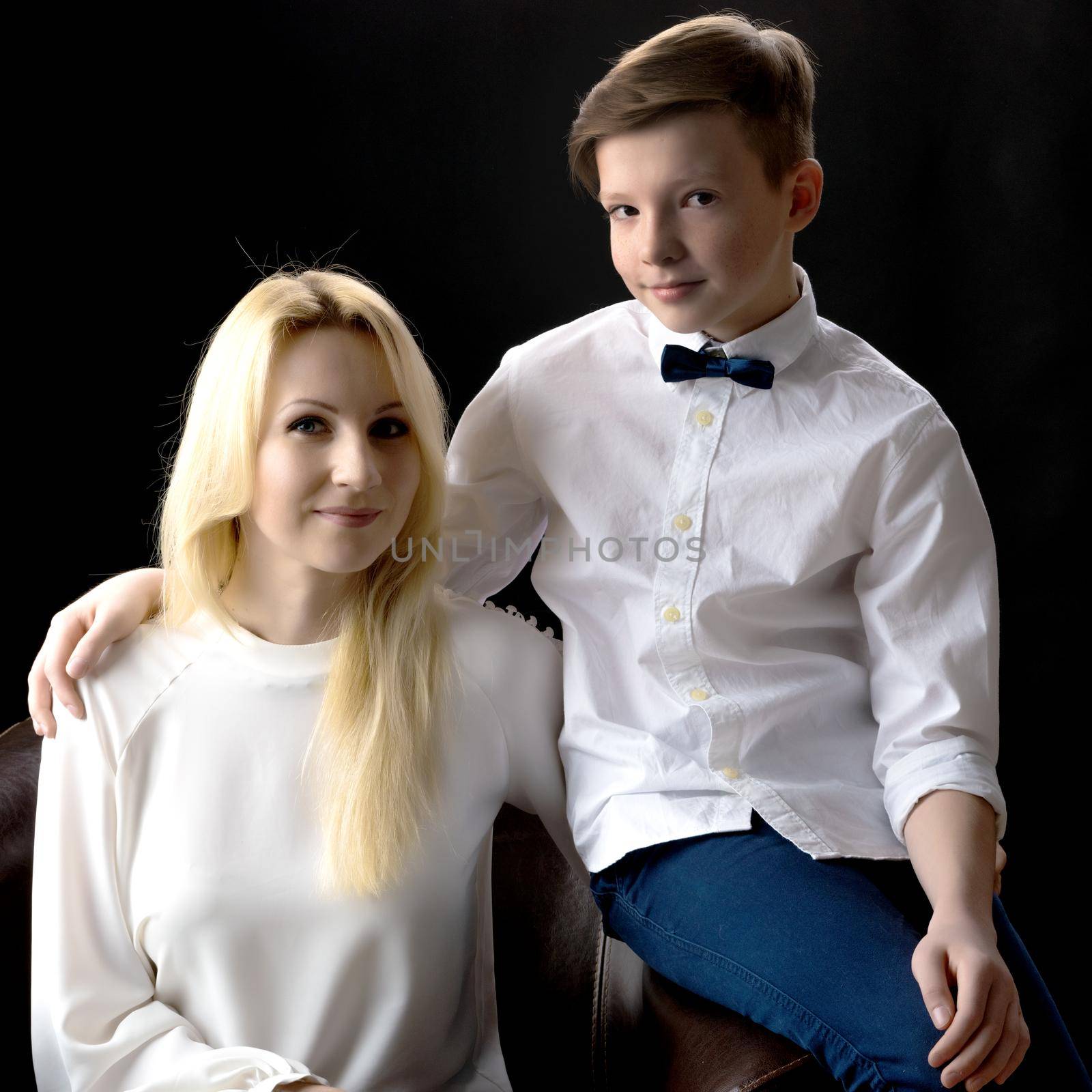 Mom and son teenager on a black background. The concept of happy childhood, People, harmonious development of the child in the family.