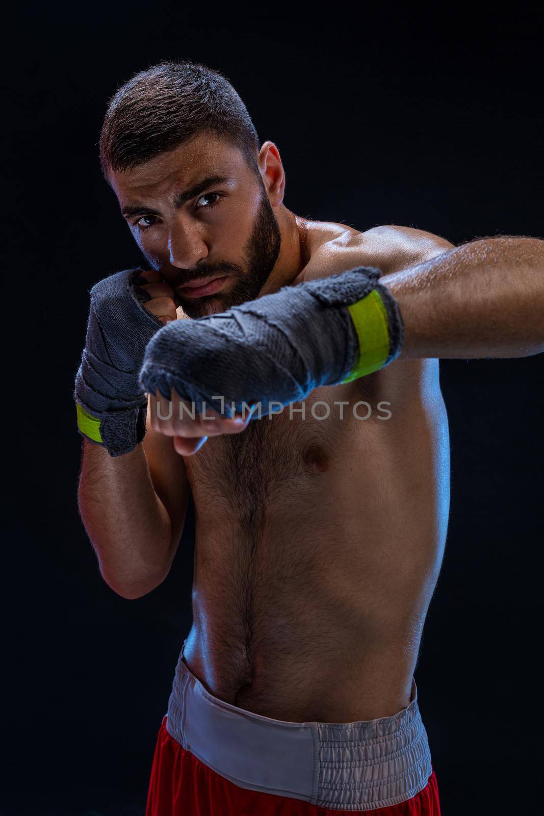 Close-up view on male hands of young athlete in gray bandages. Boxer man getting ready for hard kickboxing training session in gym. Black background. Vertical