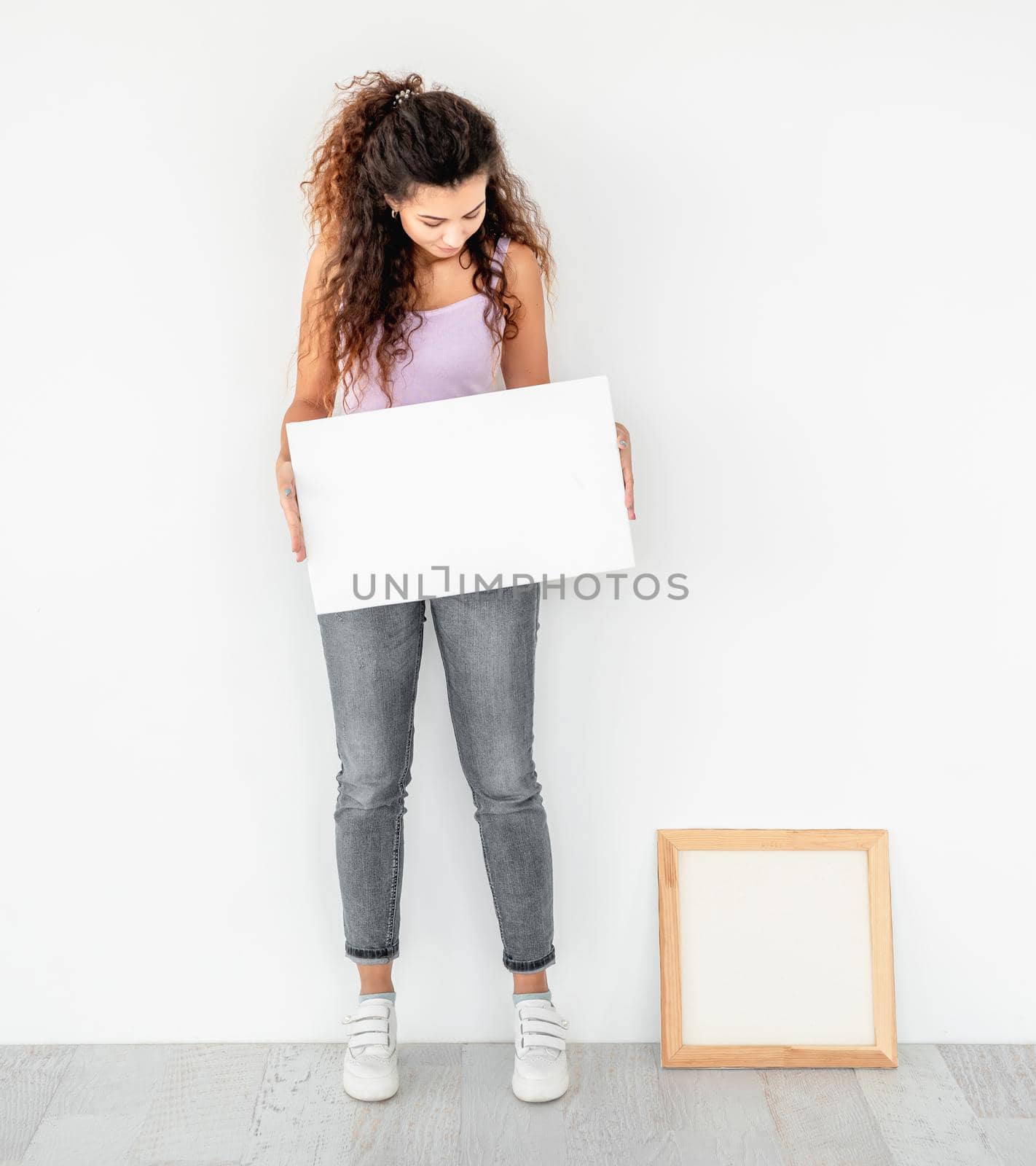 Cute girl standing near frame with empty canvas in her hands