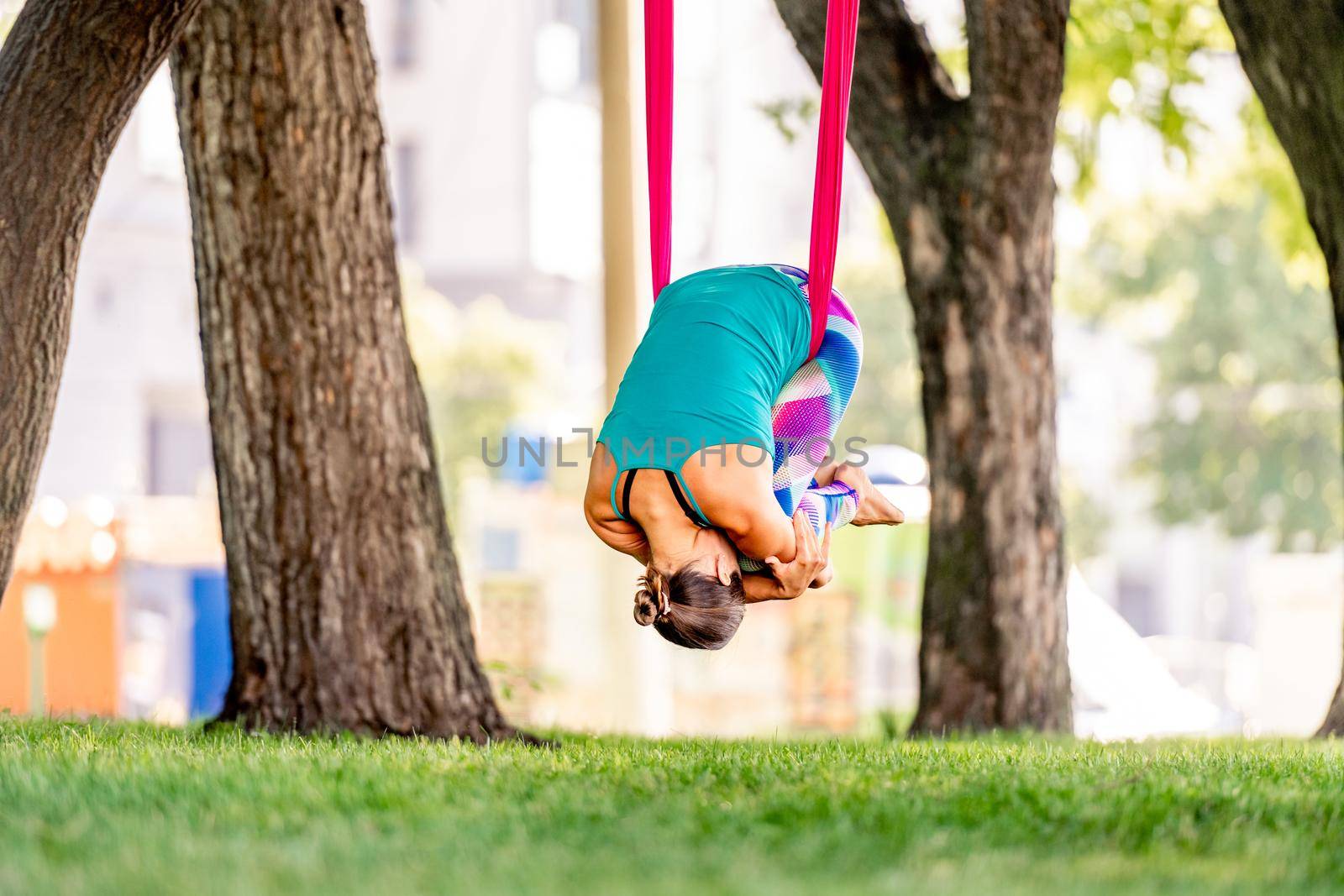 Sport girl practicing fly yoga in hammock at nature and staying in child pose in the air. Young woman doing aero fitness gymnastic stretching outdoors