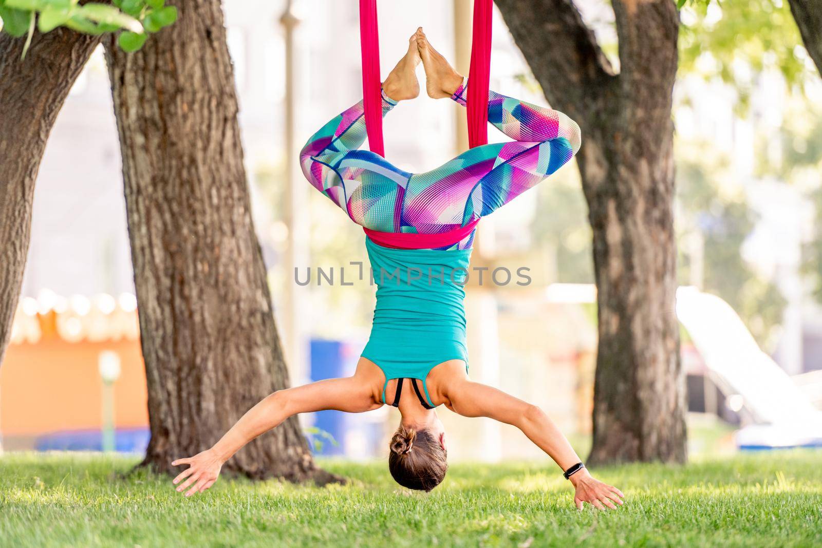 Sport girl practicing fly yoga in hammock at nature and stretching her back in the air. Young woman doing aero gymnastics outdoors back portrait