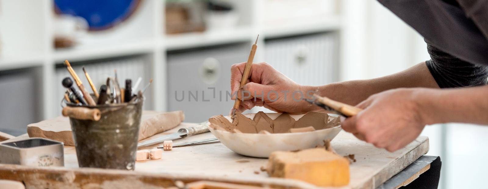 Woman potter using carving tool on plate mold at workshop
