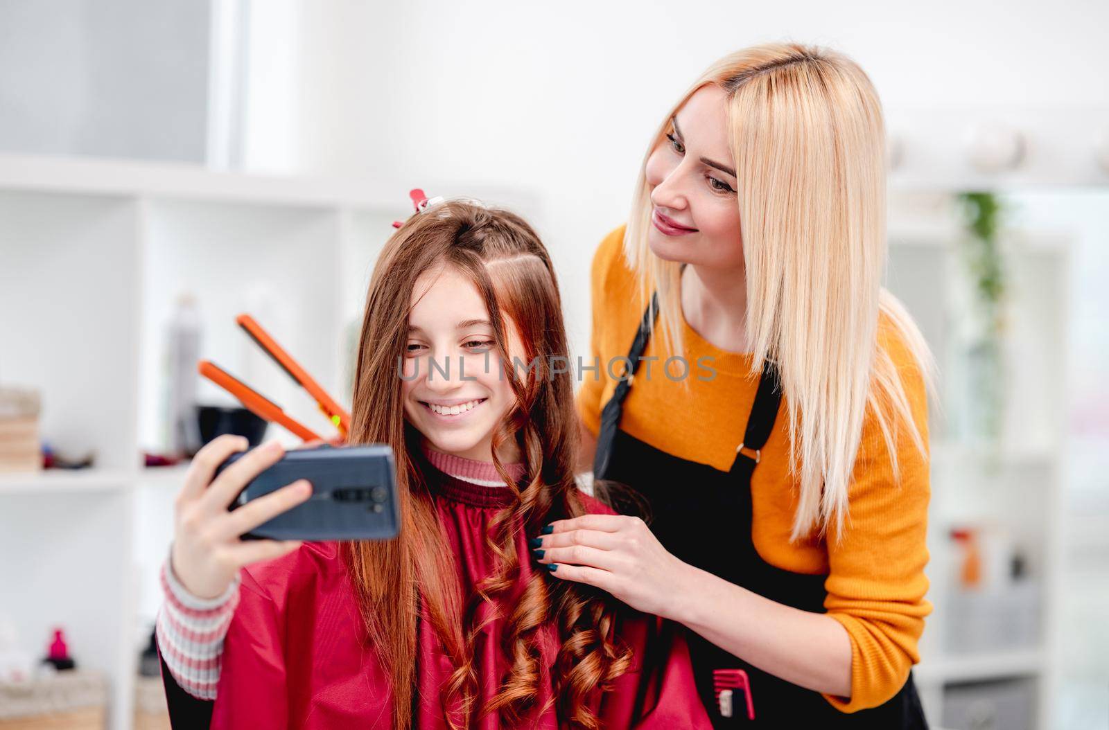 Selfie of beautiful young model with hairdresser blond woman during making curls hairstyle