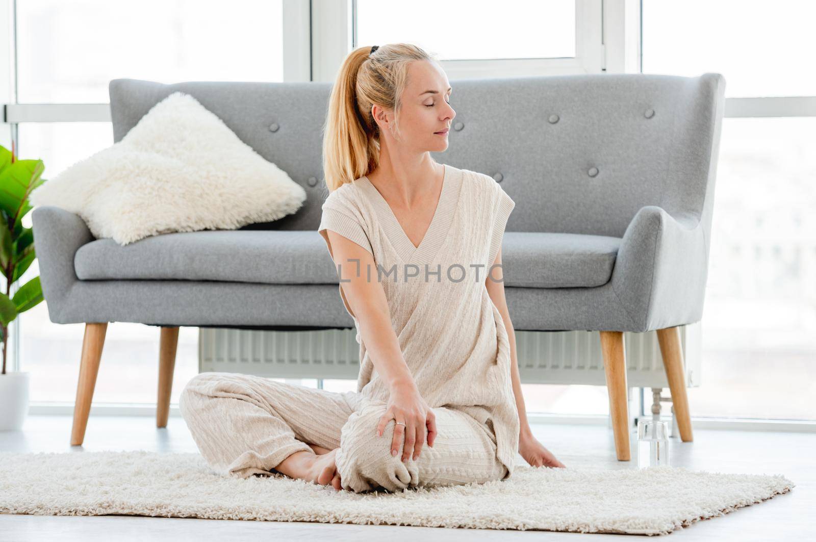 Blond girl turned to the side and stretch her back during morning yoga workout at home