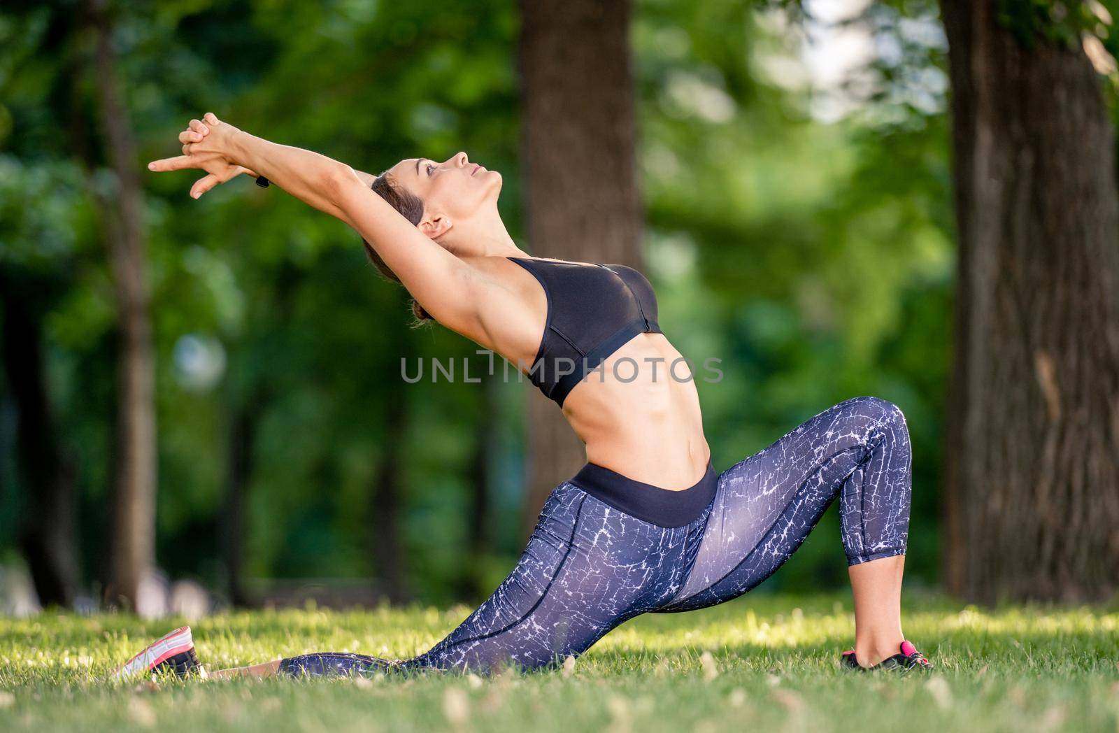 Pretty girl during yoga morning workout at the nature standing in pose and stretching her les and back. Sport woman exercising outdoors in summertime