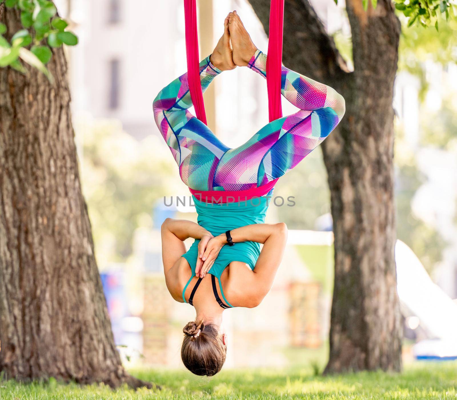 Sport girl practicing fly yoga in hammock at nature and stretching her body in the air. Young woman doing aero gymnastics outdoors