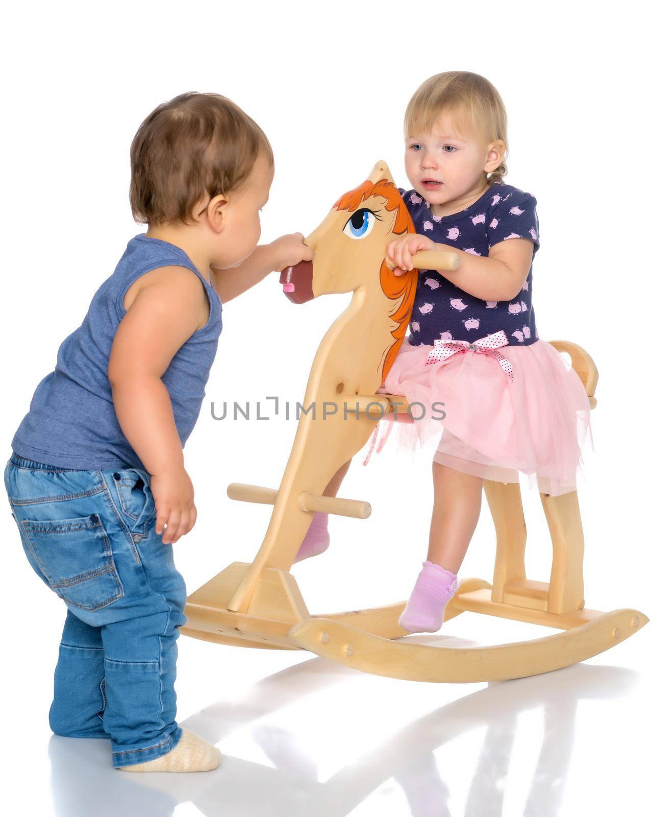 Toddler boy and girl playing with a wooden horse. by kolesnikov_studio