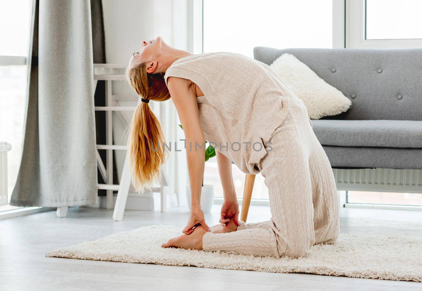 Beautiful young girl making yoga exercices for back flexibility in sunny room