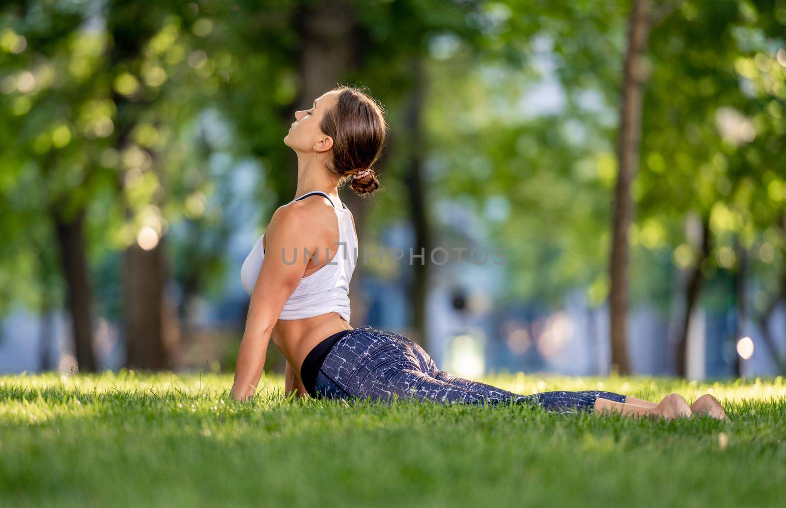 Beautiful girl doing yoga at nature and standing in upward dog pose in the park. Young woman exercising and stertching in summer