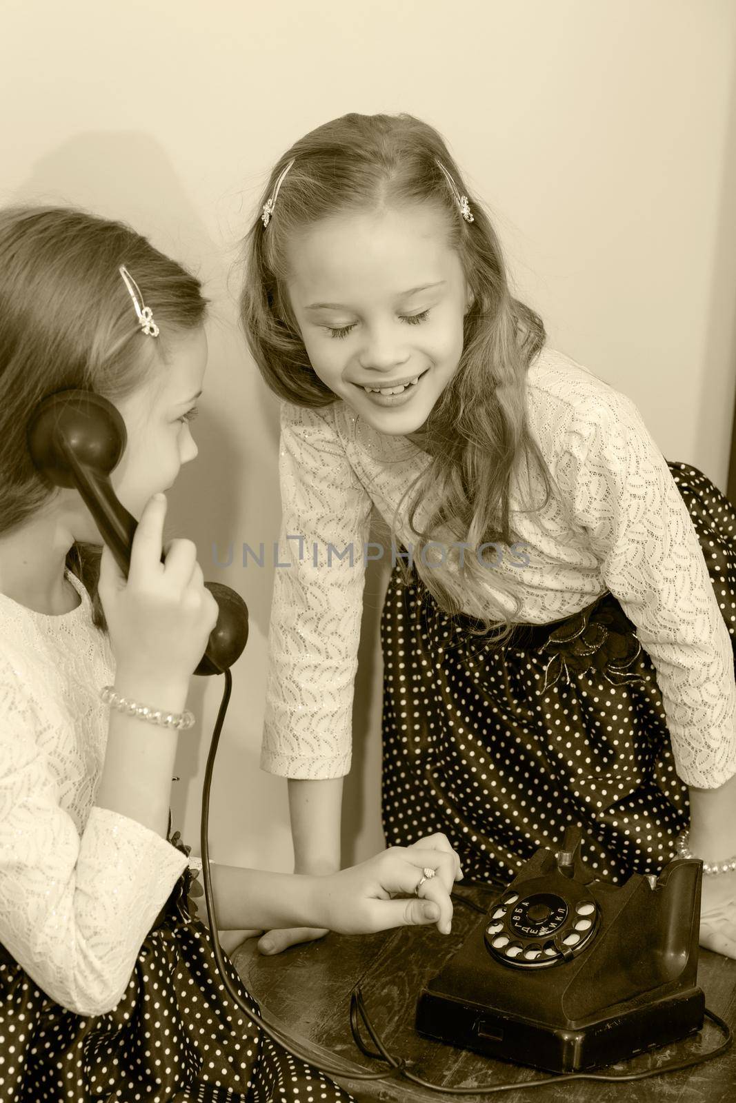 Two elegant girls sisters in beautiful dresses, talking on old phone. Retro style.Black-and-white photo. Retro style.