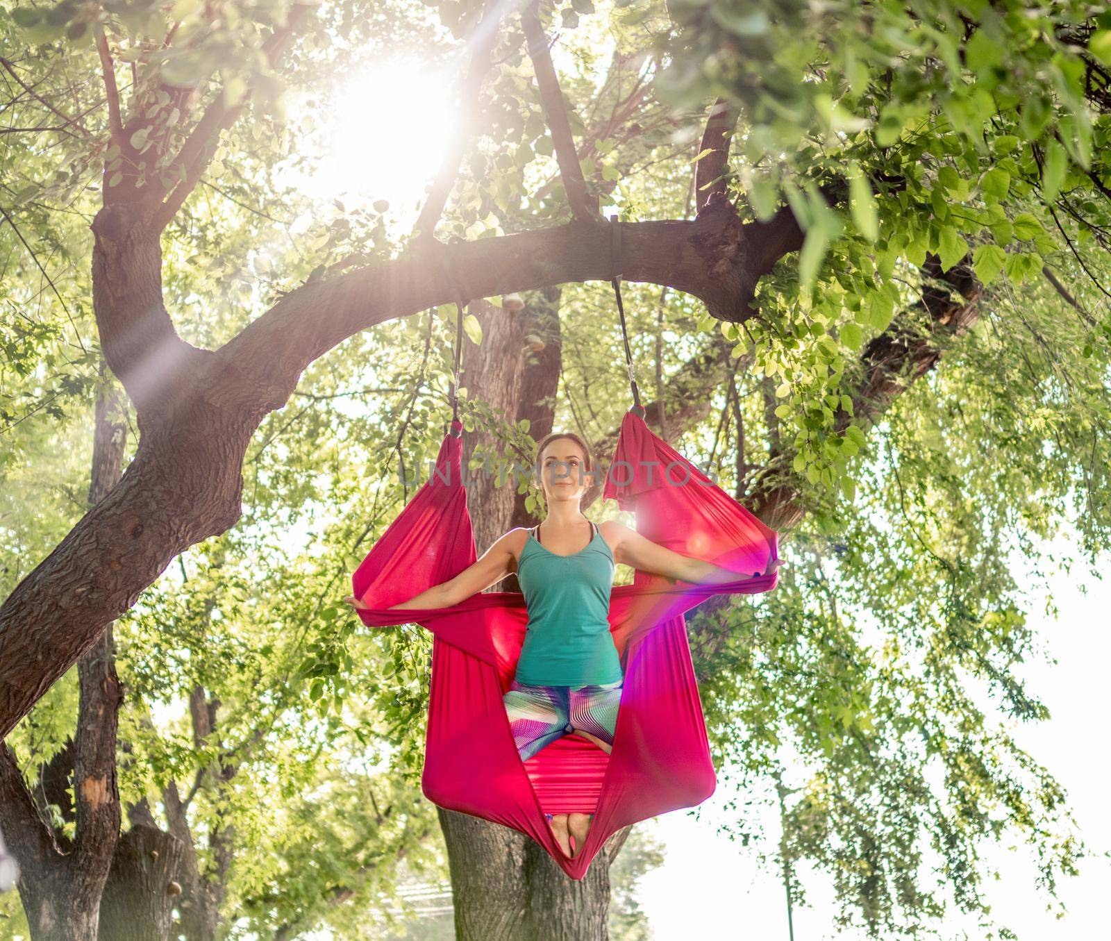 Sport girl doing fly yoga in hammock at nature keeping body in the air. Athlete woman during aero gymnastics outdoors