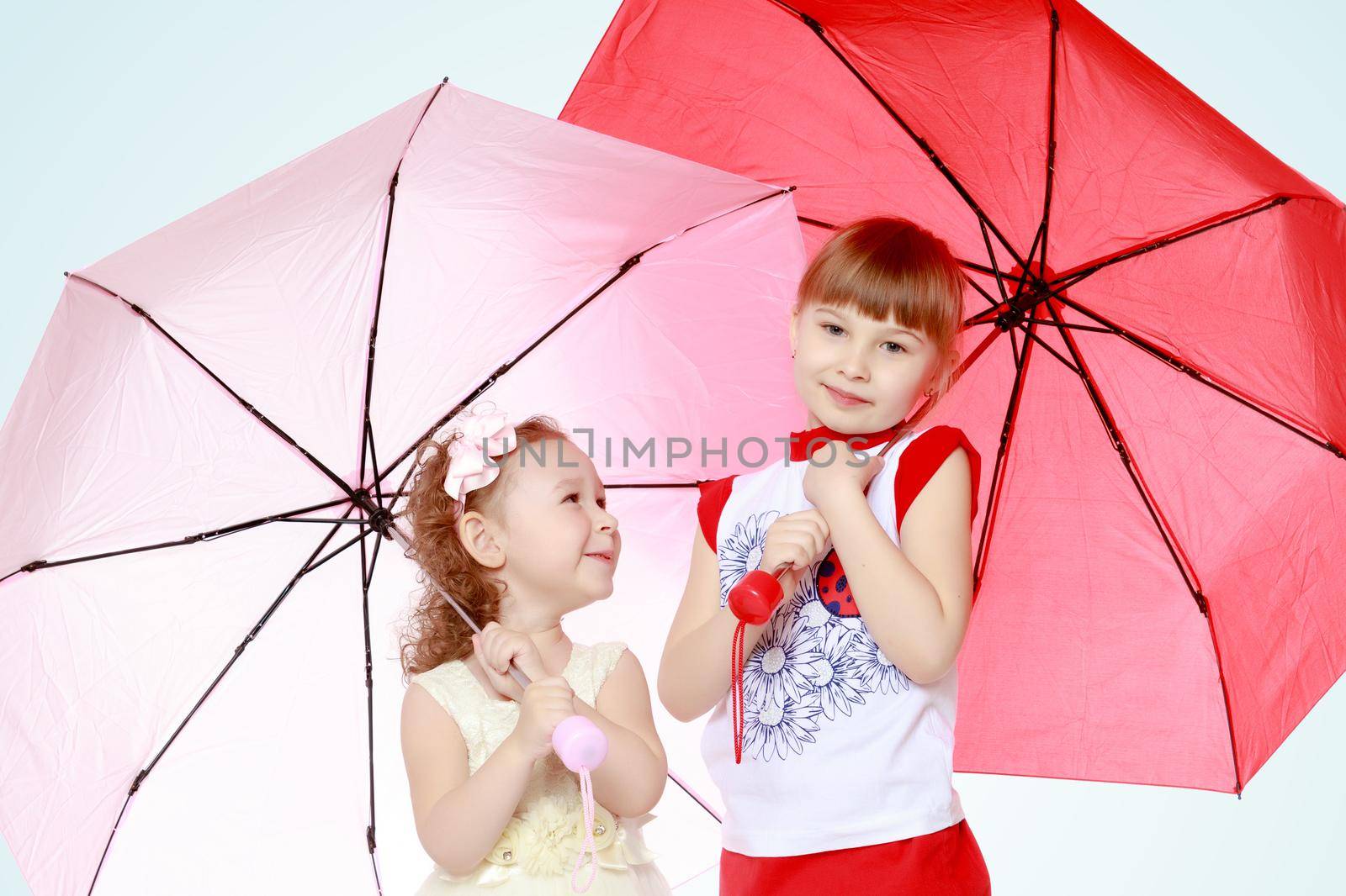 Two charming little girls, little sister and the eldest, sheltered from rain or sun under umbrellas.