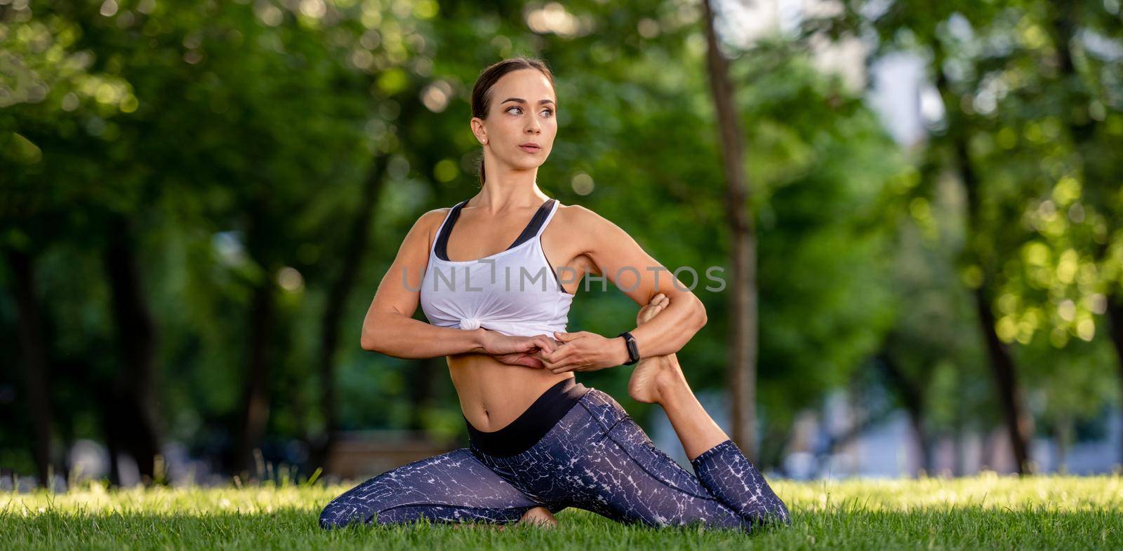 Sport girl during yoga workout at the nature stretching her legs in the morning. Young woman doing fitness exercises
