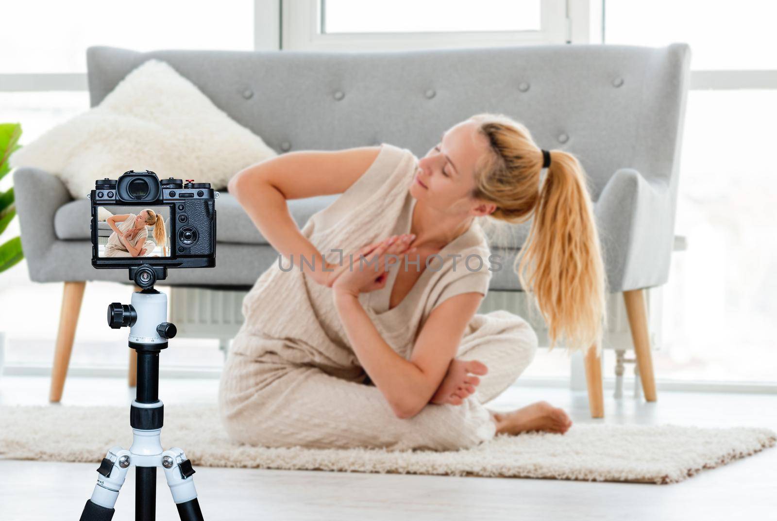 Blond girl sitting in yoga asana on the floor in the room with sunlight. Home stretching workout. Blogger profession. Shooting with a camera for a blog