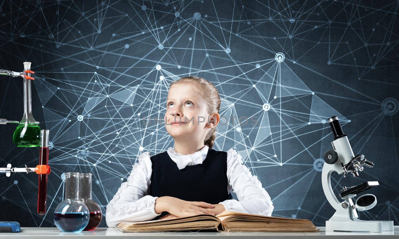 Smiling schoolgirl sitting at desk with open book. Happy girl scientist studying in classroom. Chemical laboratory with glass flasks and test tubes. Clever girl in schoolwear reading book.