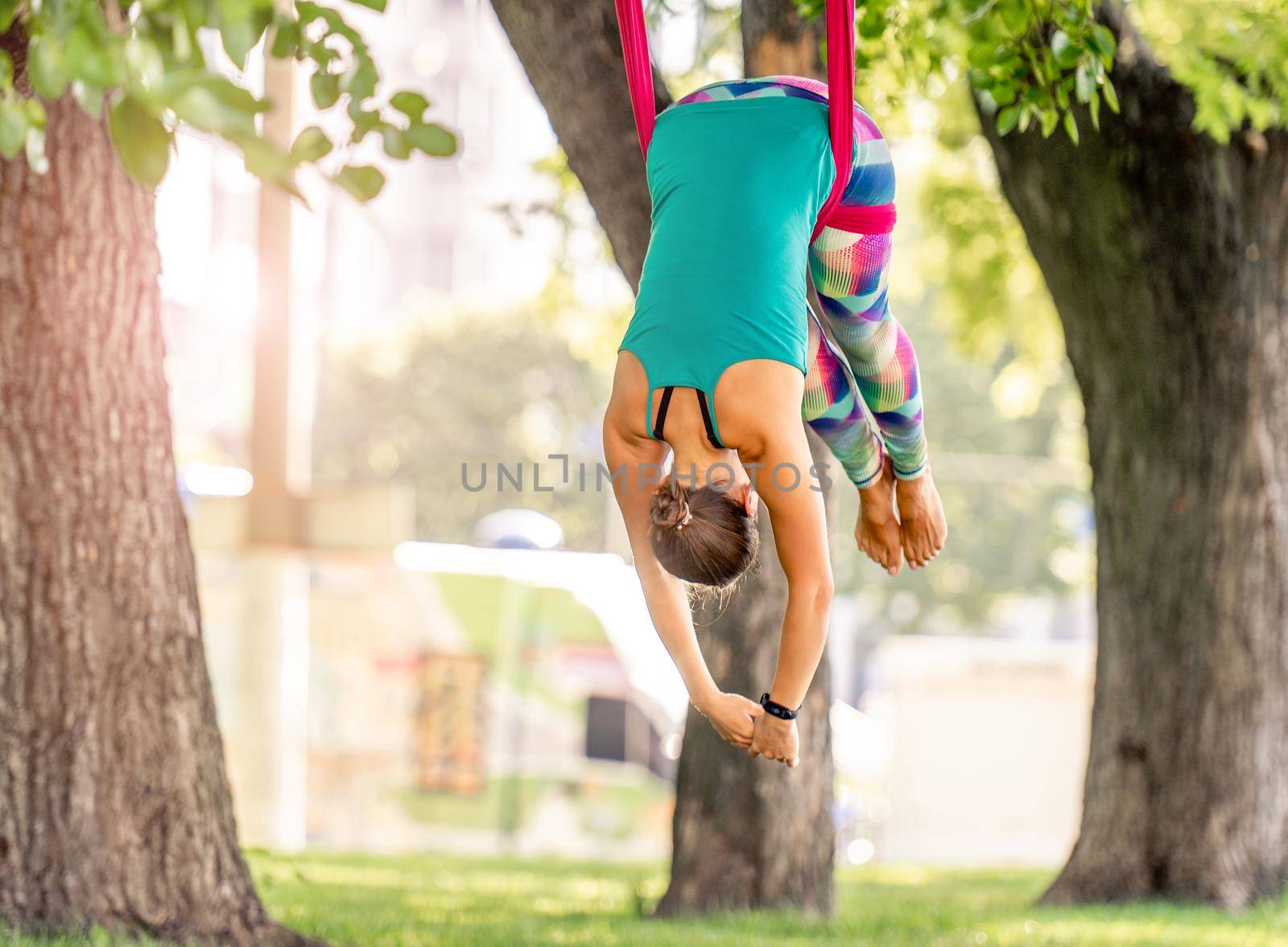 Girl during fly yoga practice in hammock stretching her body at nature and keeping balance in the air. Young woman doing aero fitness gymnastic exercising outdoors