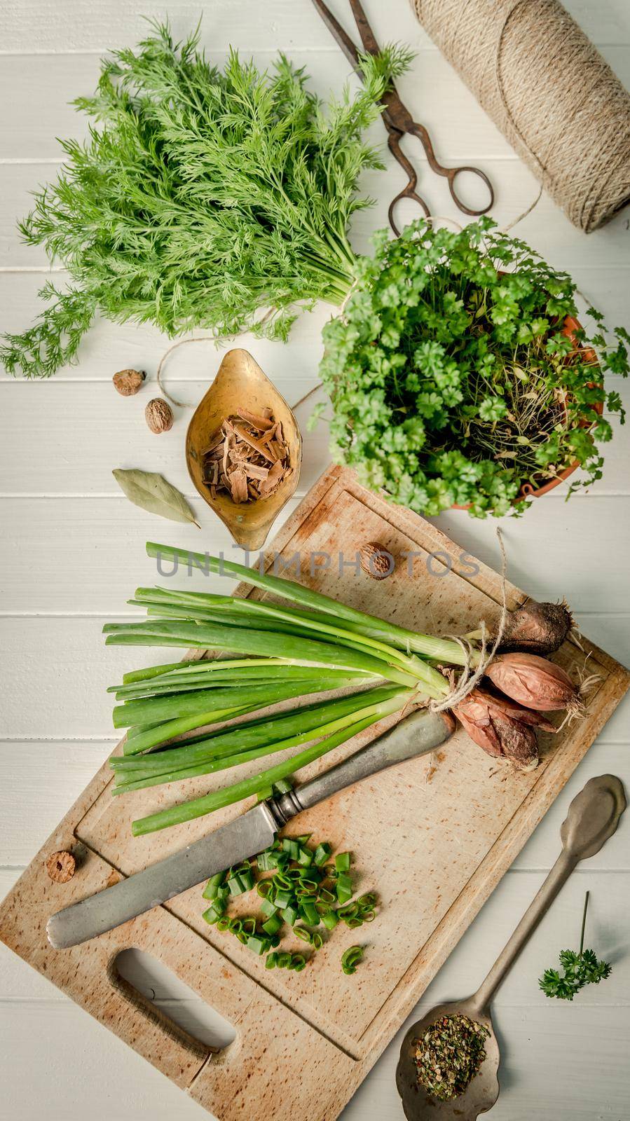 Green onion, dill on the cutting board, rustic silverware on table, spices, preparation process, topshot
