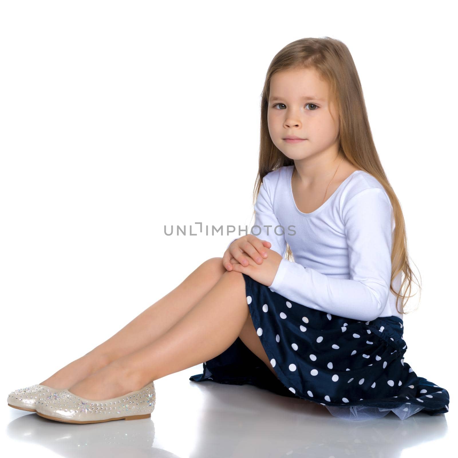 Beautiful little girl is sitting on the floor in the studio. The concept of a happy childhood, beauty and fashion. Isolated on white background.